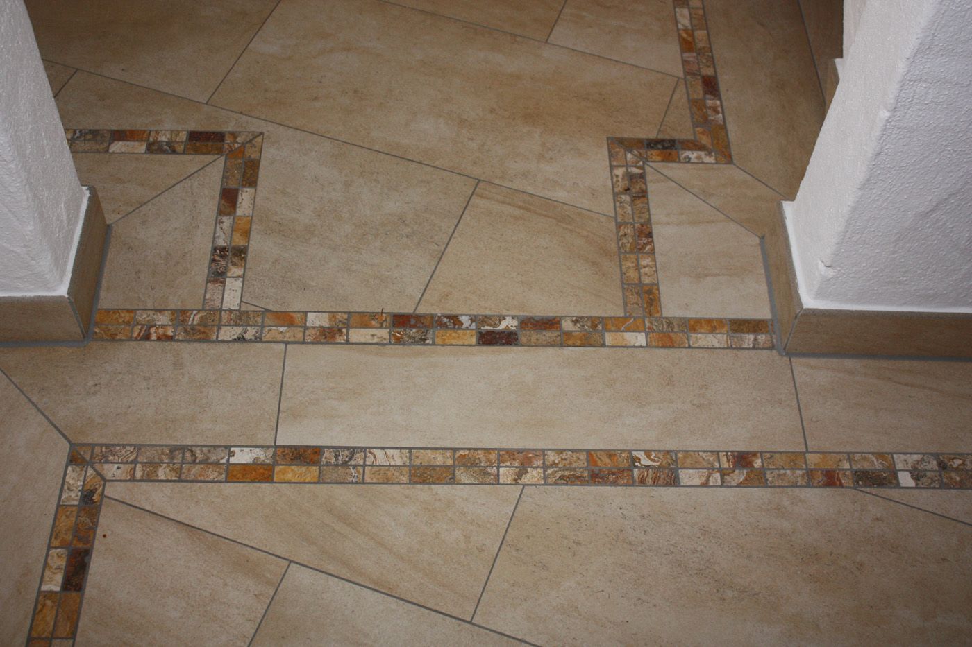 Bodenbelag aus großformatigen beigen Fliesen mit Mosaikbordüre.