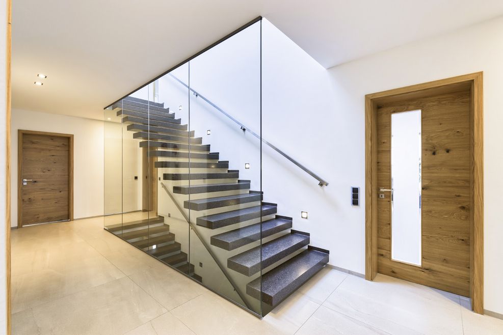 Geradläufige Treppe mit dunklen Stufen und Glasscheibe als Absturzsicherung.